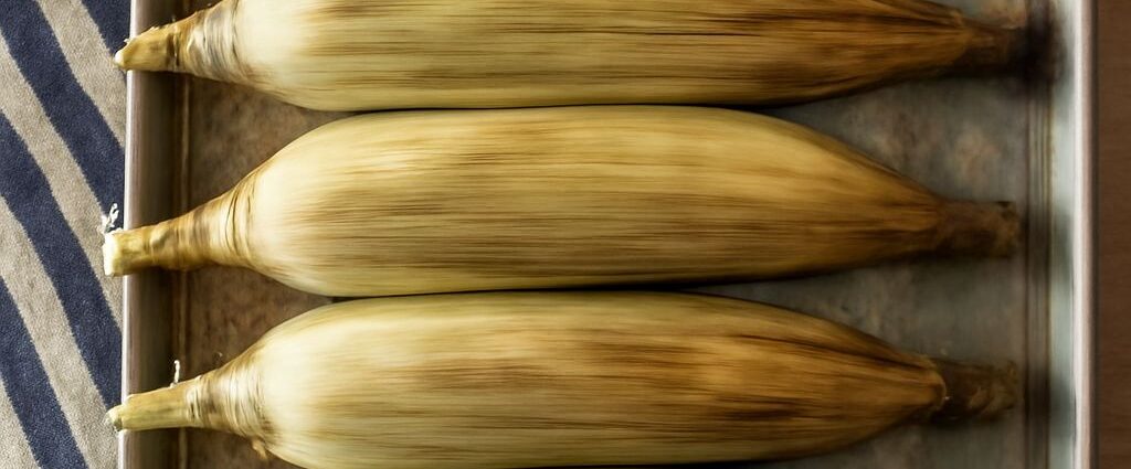 Oven roasted corn on the cob in husk on a baking tray