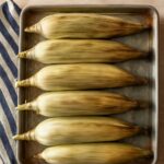 Oven roasted corn on the cob in husk on a baking tray