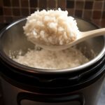 Sushi rice in a rice cooker with a wooden spoon