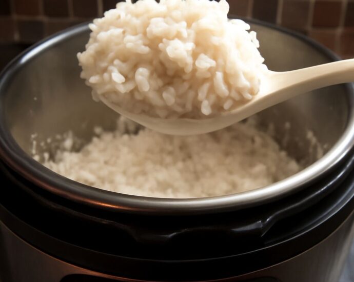 Sushi rice in a rice cooker with a wooden spoon