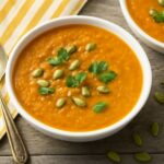 Smooth recipe for carrot soup topped with herbs in a bowl