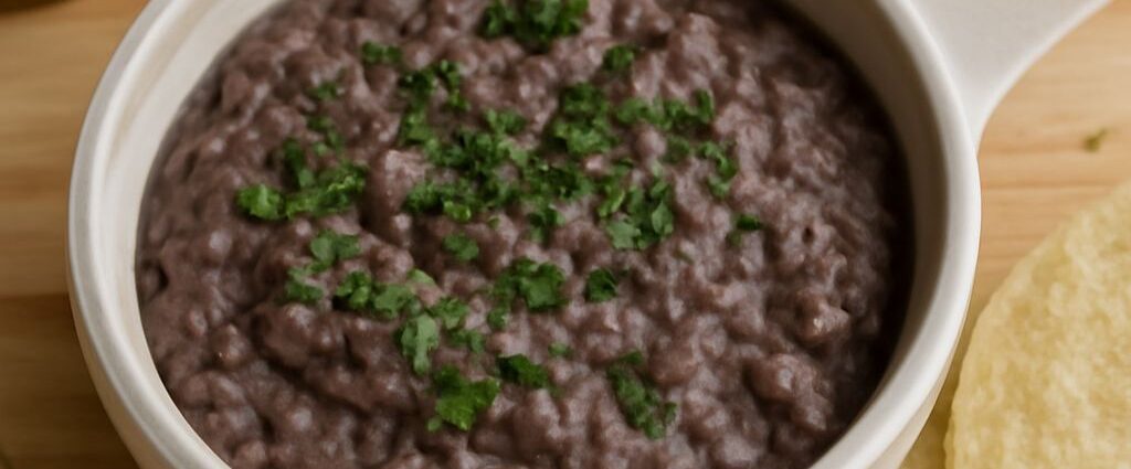 Mashed black beans in a bowl beside warm tortillas