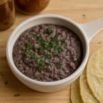Mashed black beans in a bowl beside warm tortillas