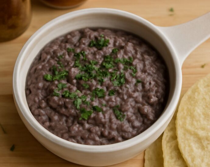 Mashed black beans in a bowl beside warm tortillas
